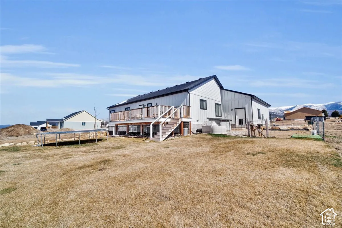 Single-story residence featuring light-colored vertical siding, dark-toned roof shingles, an elevated wood deck, and mountain backdrop