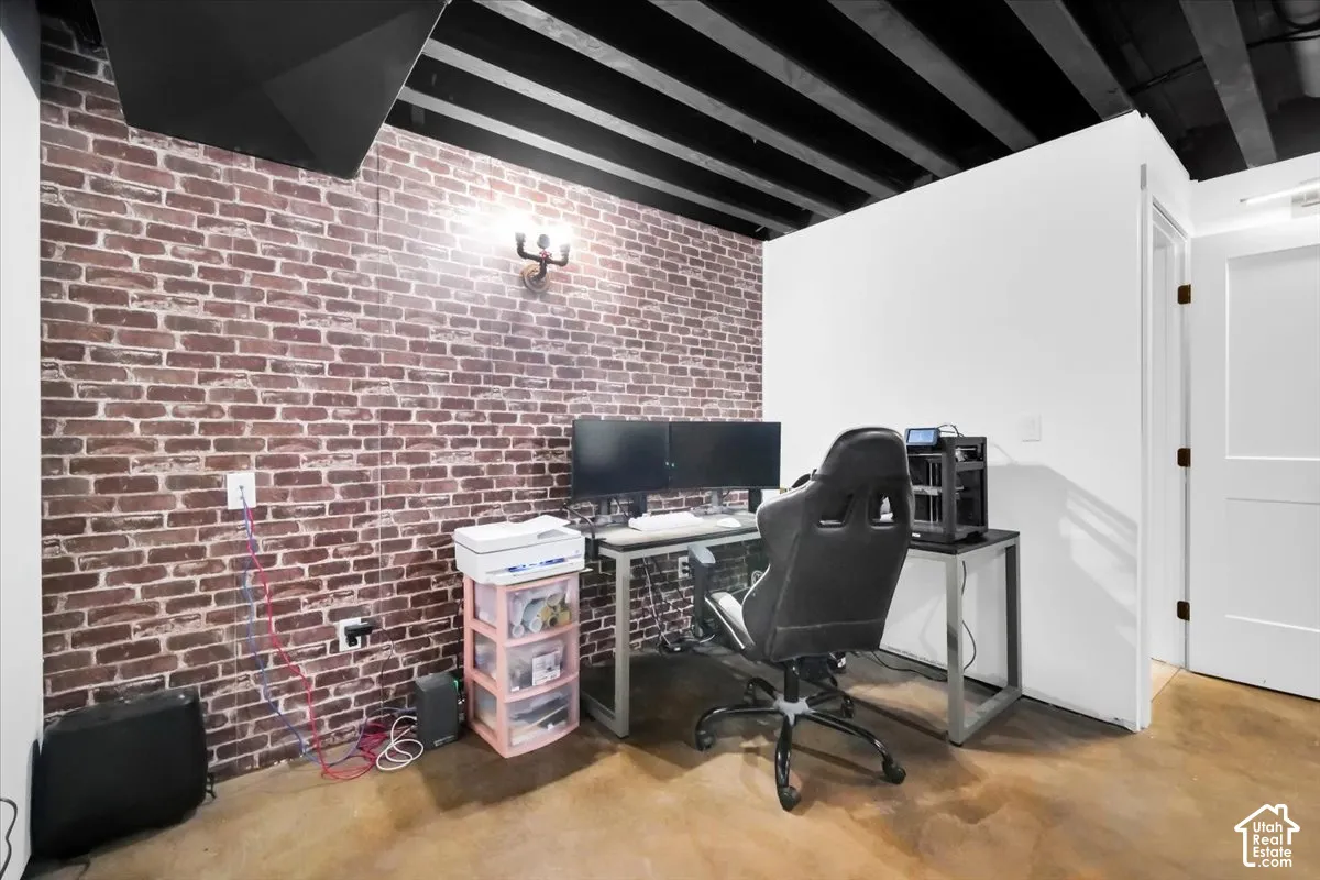 Exposed ceiling joists painted black, exposed brick wall, concrete flooring, and a single-panel interior door