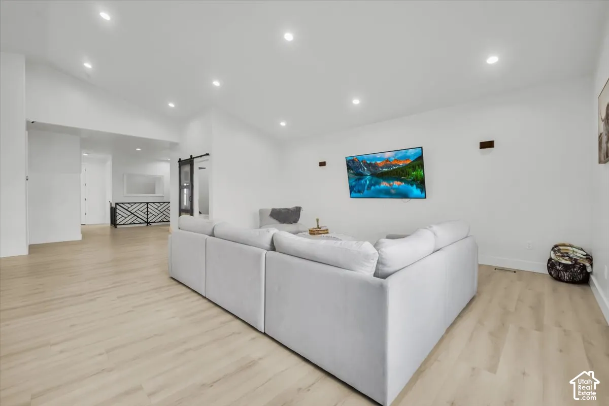 Open-concept interior featuring light wood-finish flooring, vaulted ceilings, recessed lighting, and a sliding barn-style door