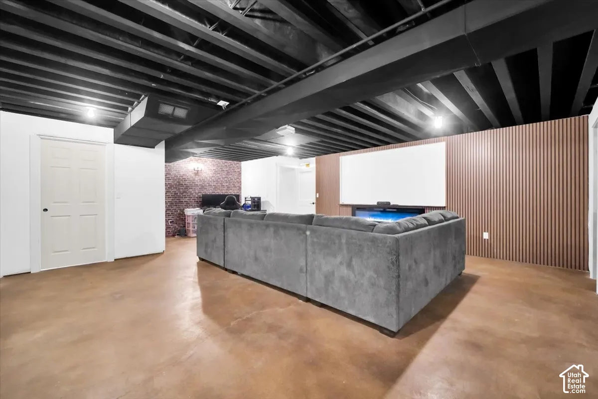 Lower level space featuring an exposed joist ceiling, concrete flooring, vertical wood-slat accent wall, and a recessed electric fireplace