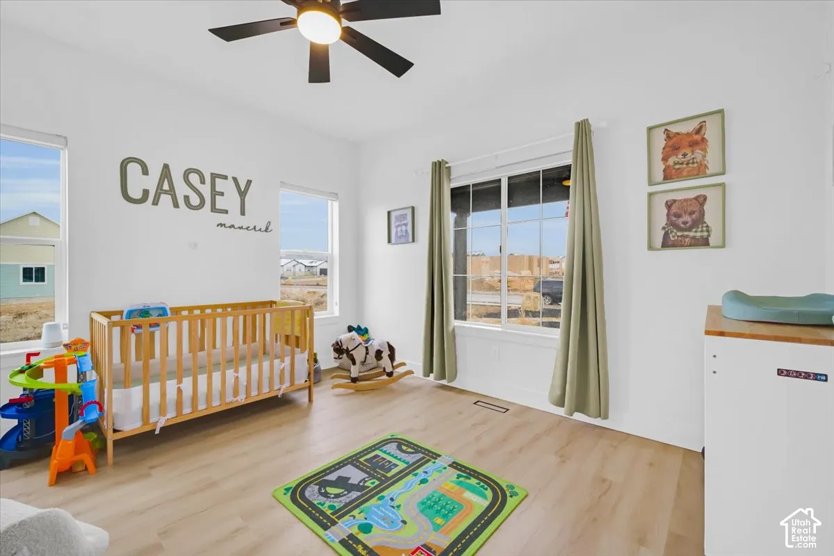 Room interior featuring wood-finish flooring, dual windows with white frames, and a ceiling-mounted light fixture with integrated fan