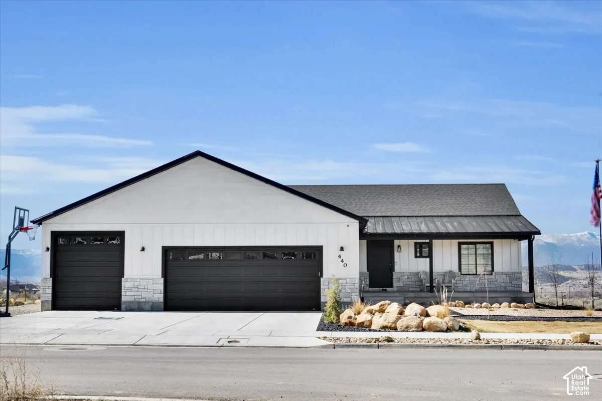 Single-level exterior featuring white vertical siding, black metal roofing, stone veneer accents, and a three-car garage