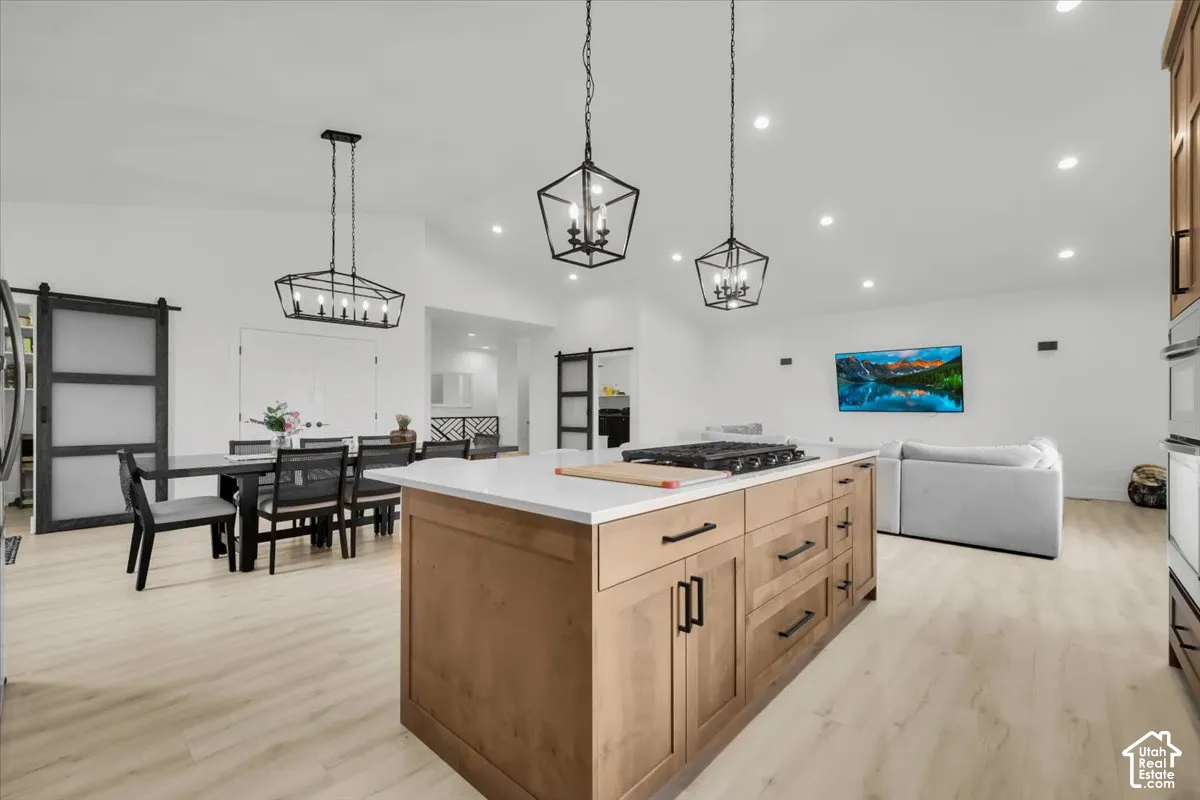 Kitchen island featuring wood-finish cabinetry, white countertop, and built-in cooktop, illuminated by geometric pendant lighting with wood-finish flooring throughout
