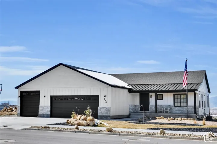 Modern farmhouse exterior featuring vertical board-and-batten siding, stone masonry accents, a dark metal roof, and a three-car garage