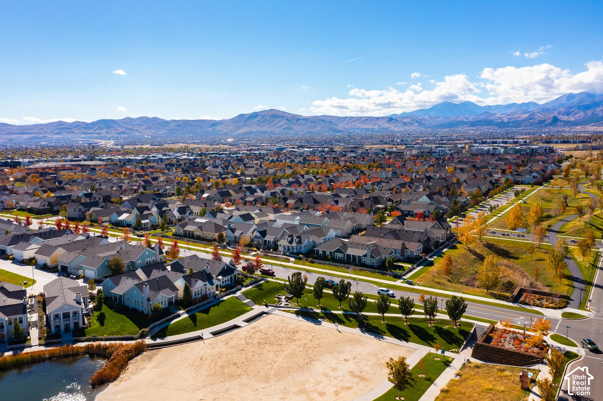 Aerial perspective featuring expansive mountain backdrops, paved walking paths, manicured green space, and a pond shoreline