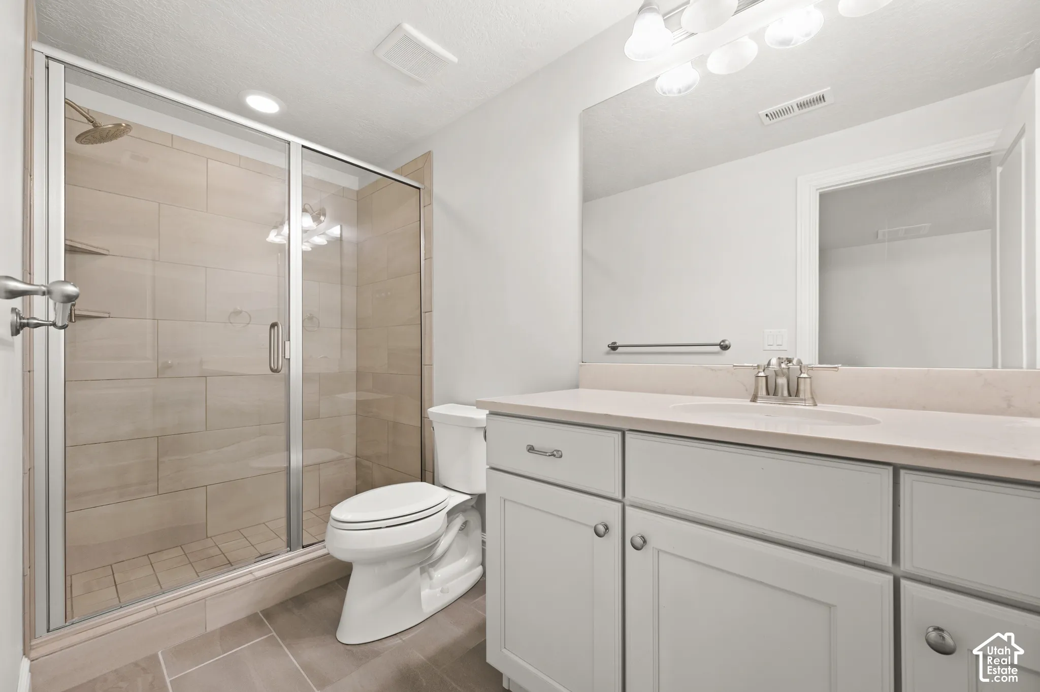 Bathroom featuring a glass-enclosed shower with large-format tile surround, light-toned cabinetry, solid surface countertop with integrated basin, and expansive wall-mounted mirror
