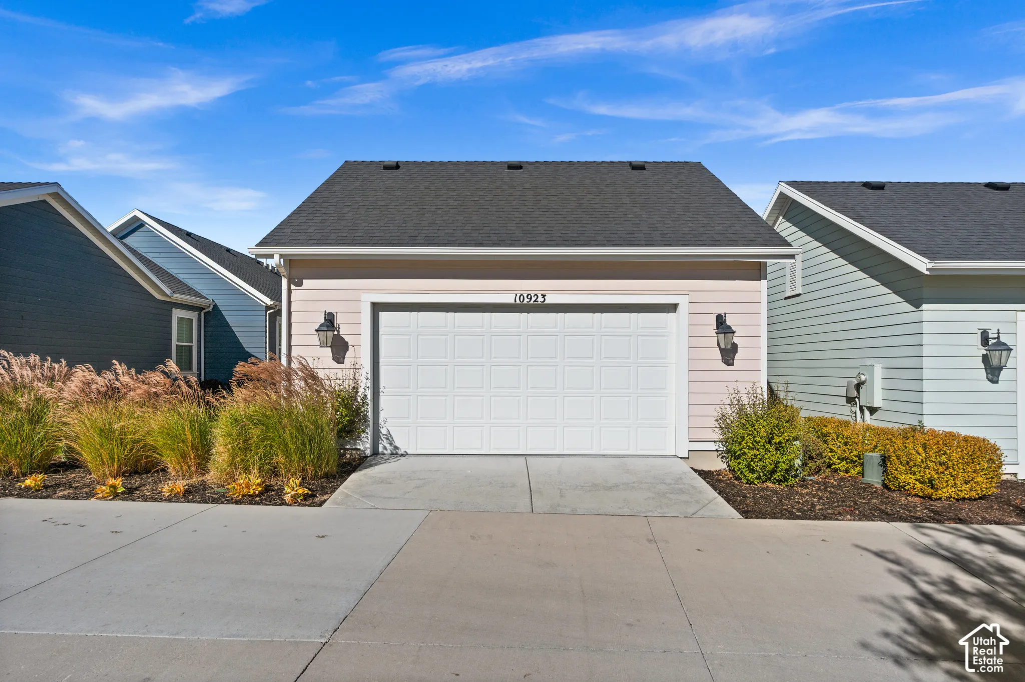 Single-car garage exterior with horizontal siding, gabled roofline, concrete driveway, and wall-mounted exterior lanterns