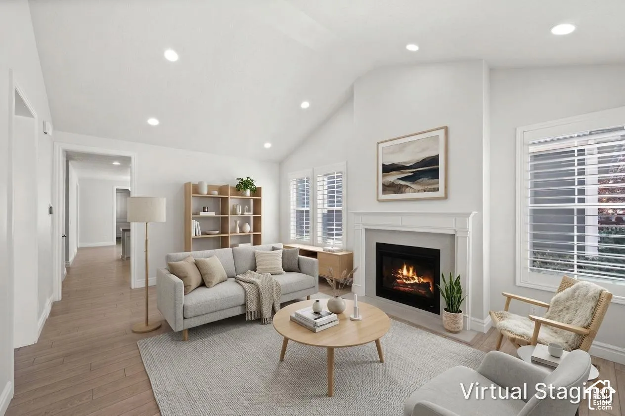 Vaulted ceiling living area featuring wood-finish flooring, recessed lighting, and a fireplace with a decorative mantel and surround