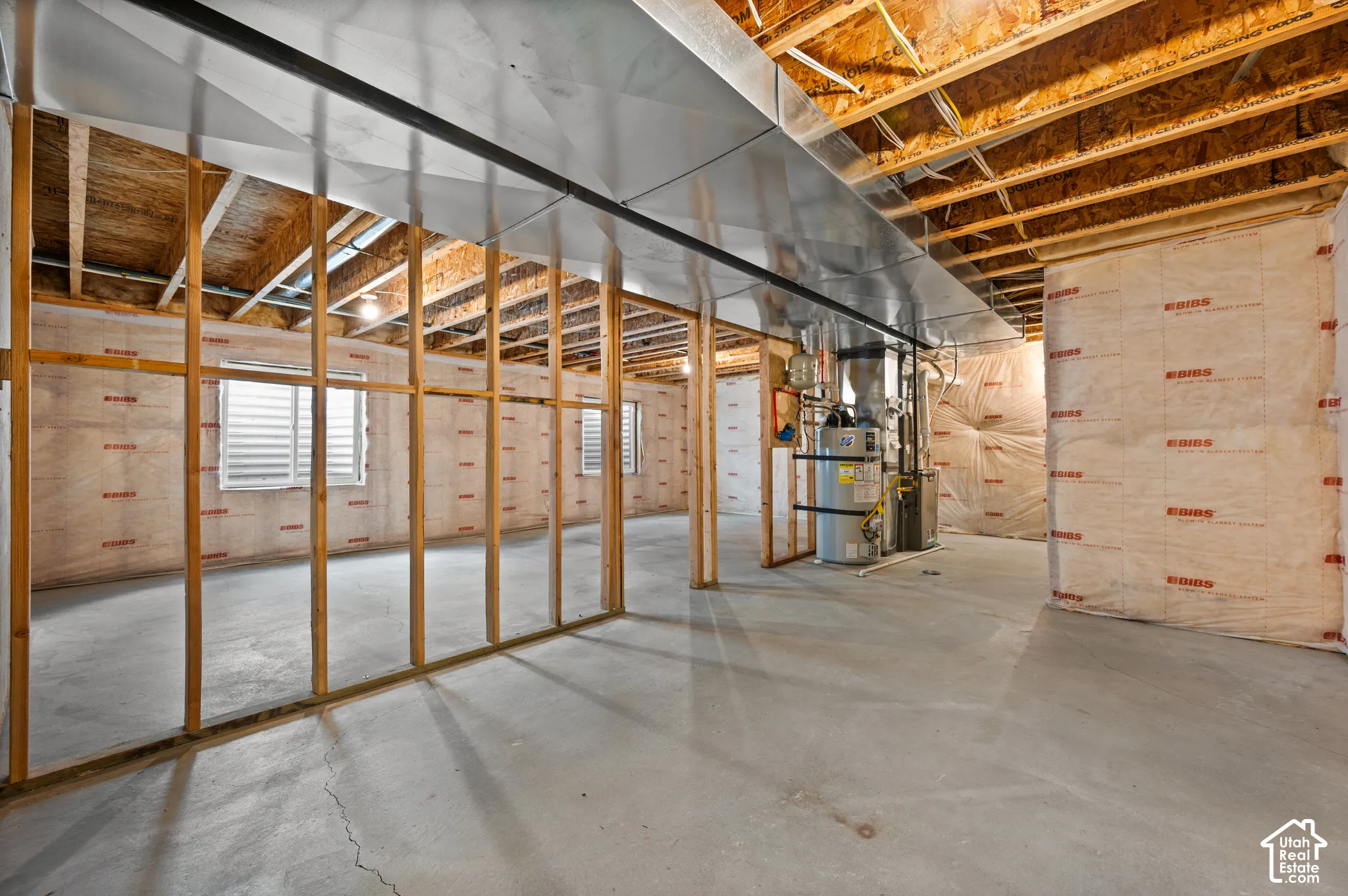 Unfinished space featuring exposed wood framing, concrete flooring, fiberglass wall insulation, metal ductwork, and a water heater