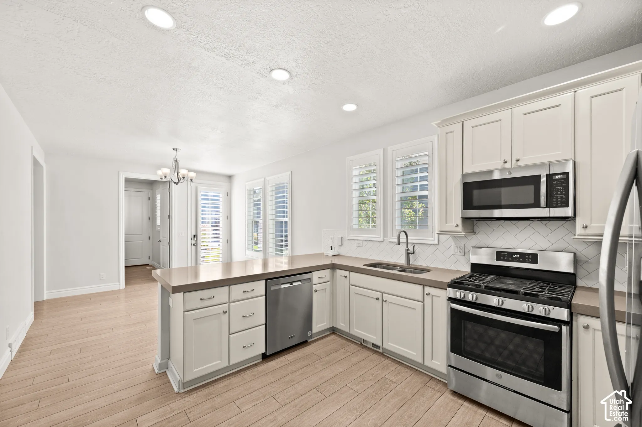 Kitchen featuring Shaker-style cabinetry, stainless steel appliances, herringbone-pattern tile backsplash, wood-finish flooring, and recessed lighting