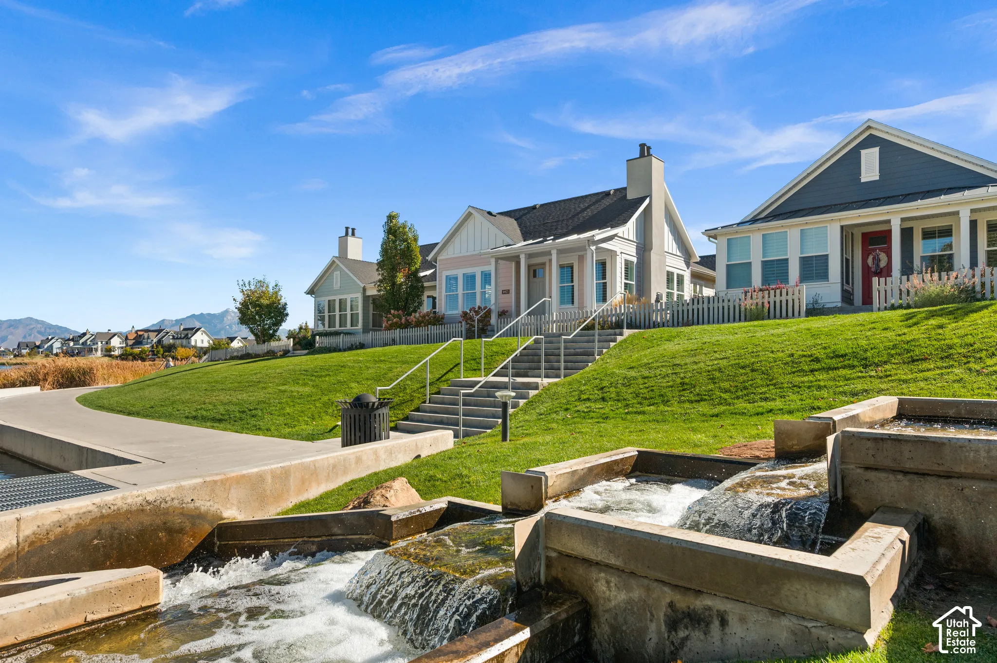 Multi-level exterior featuring vertical siding, stone masonry chimneys, tiered concrete water features, paved walkways, and metal handrails