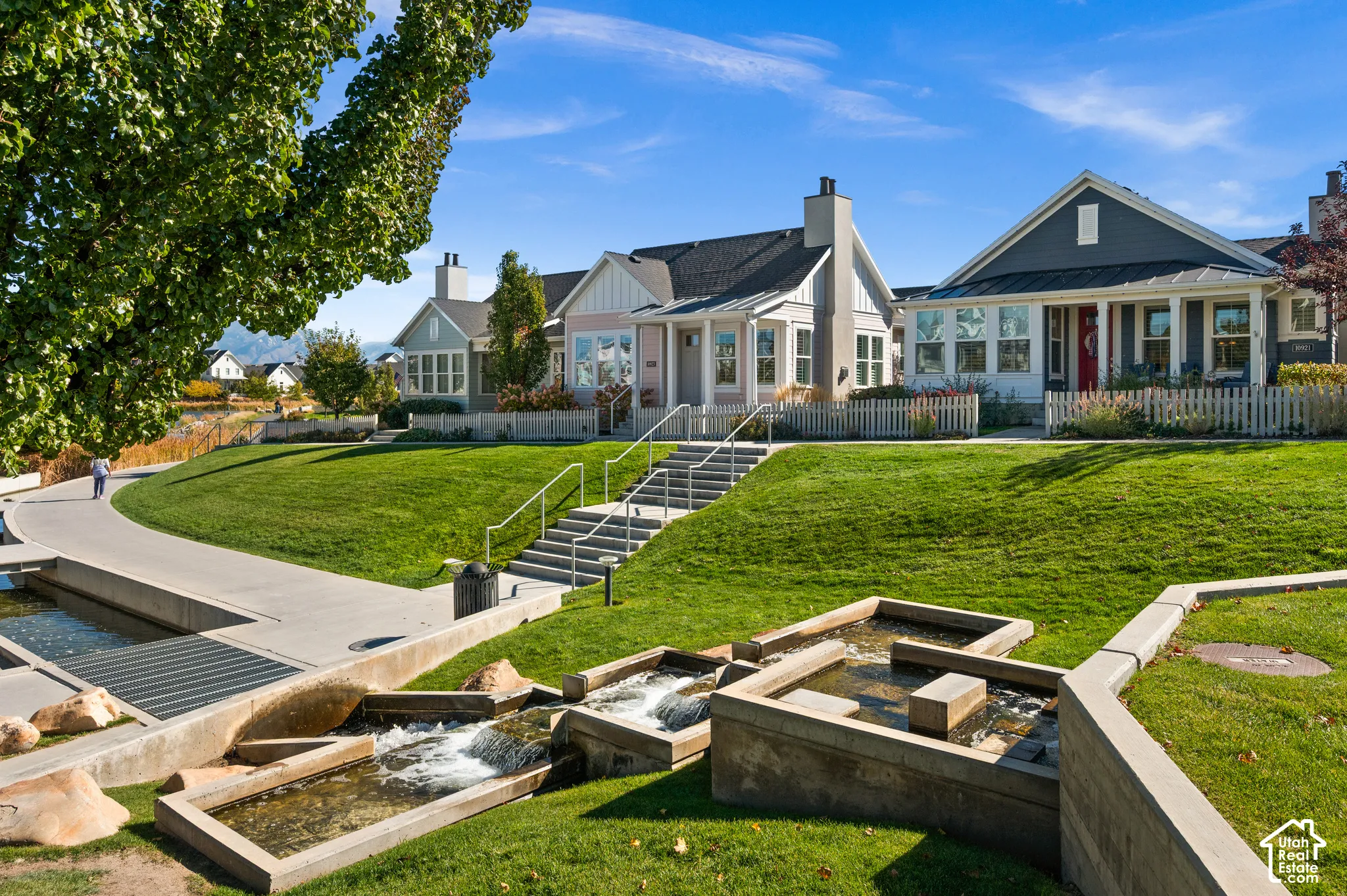 Exterior featuring multi-gabled rooflines, fiber cement siding, white picket fencing, stepped concrete hardscaping, and a tiered water feature