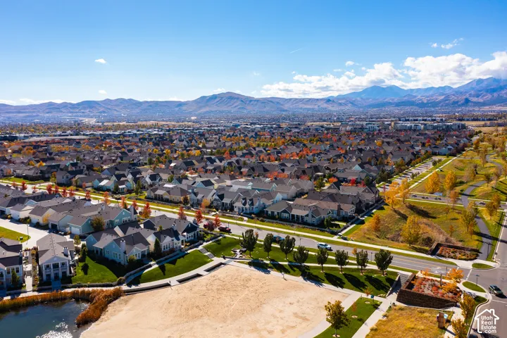 Aerial perspective featuring expansive mountain backdrops, paved walking paths, manicured green space, and a pond shoreline