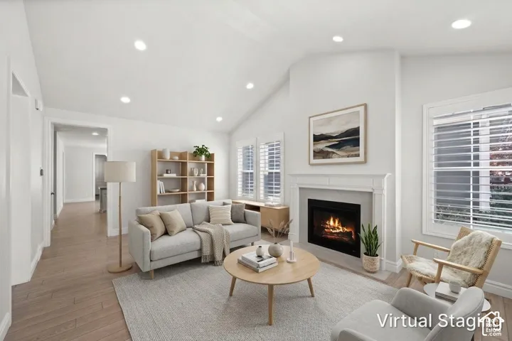 Vaulted ceiling living area featuring wood-finish flooring, recessed lighting, and a fireplace with a decorative mantel and surround