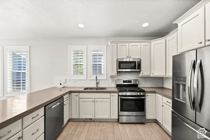 Kitchen featuring white Shaker-style cabinetry, solid-surface countertops, a herringbone-patterned tile backsplash, stainless steel appliances, and wood-finish flooring