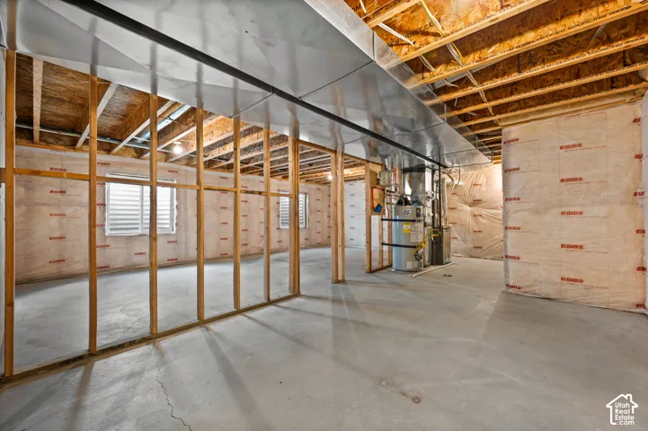 Unfinished space featuring exposed wood framing, concrete flooring, fiberglass wall insulation, metal ductwork, and a water heater
