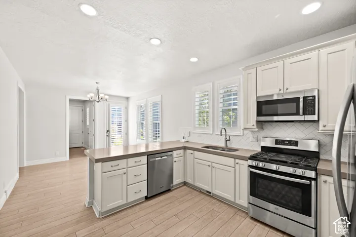 Kitchen featuring Shaker-style cabinetry, stainless steel appliances, herringbone-pattern tile backsplash, wood-finish flooring, and recessed lighting