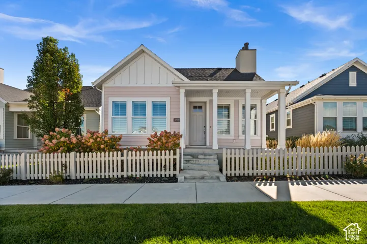 Single-story residence featuring vertical board-and-batten siding, a covered front porch with square columns, a steep-pitched roofline, and a classic white picket fence