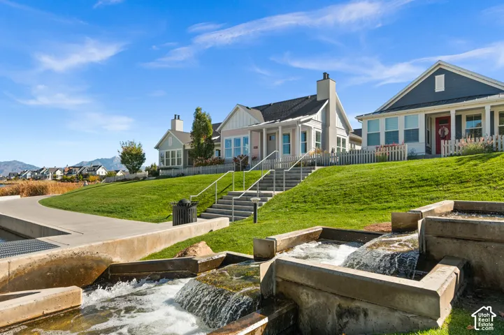 Multi-level exterior featuring vertical siding, stone masonry chimneys, tiered concrete water features, paved walkways, and metal handrails