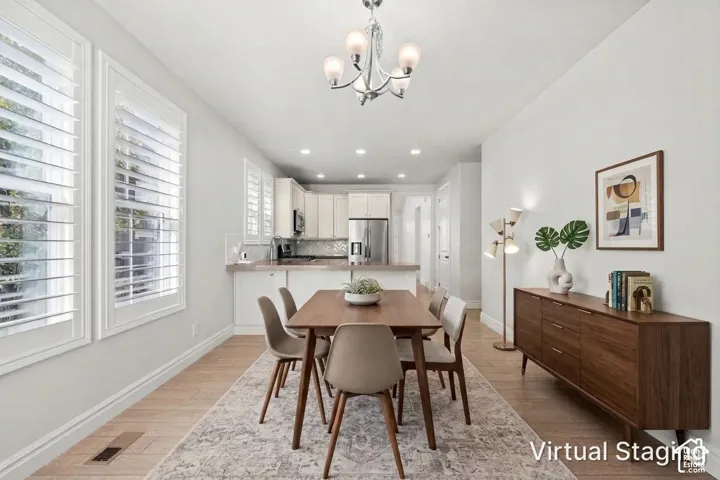Open-concept space featuring wood-finish flooring, plantation shutters, a five-arm metal chandelier, recessed lighting, and white cabinetry