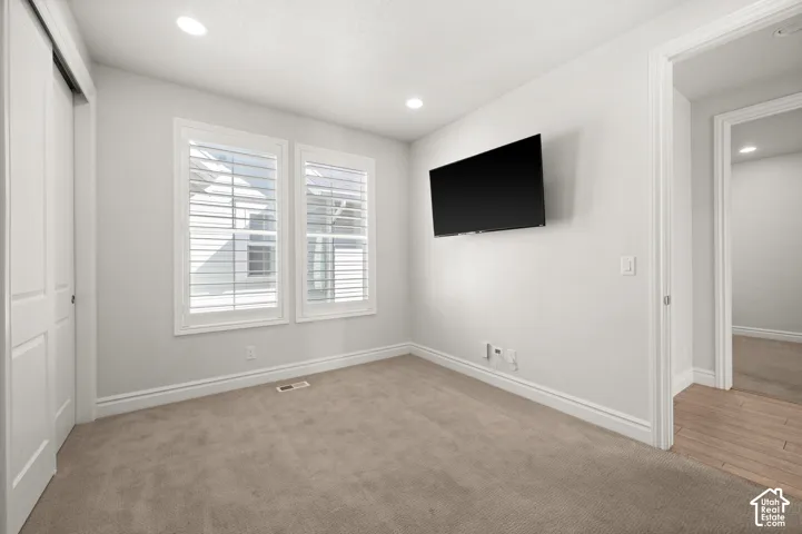 Interior space featuring neutral-toned carpeting, recessed lighting, dual windows with white plantation shutters, and multi-panel interior doors