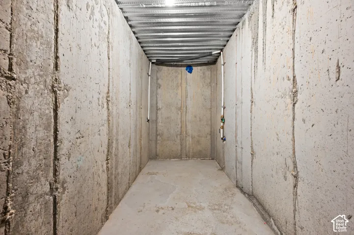 Unfinished storage space featuring poured concrete walls, a concrete floor, and a corrugated metal ceiling