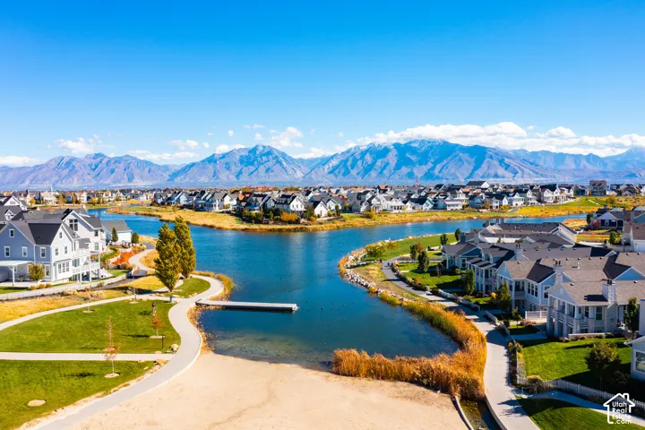 Aerial perspective featuring a central pond, sandy shoreline, concrete walking paths, mature landscaping, and a mountain backdrop