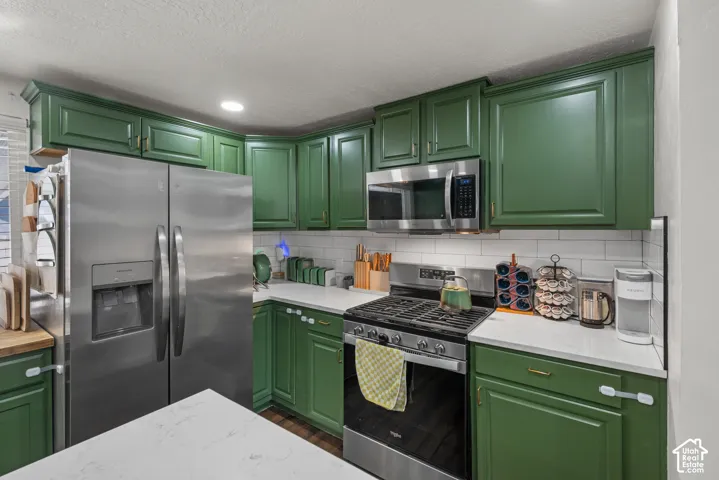 Kitchen featuring green cabinetry, stainless steel appliances, white subway tile backsplash, and quartz countertops