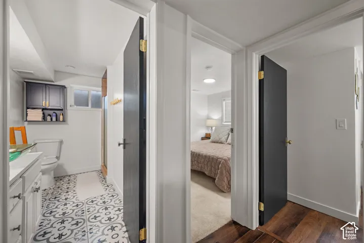 Bathroom featuring patterned floor tile, white shaker-style vanity cabinetry, wall-mounted dark-toned upper cabinetry, and dark-finished interior doors