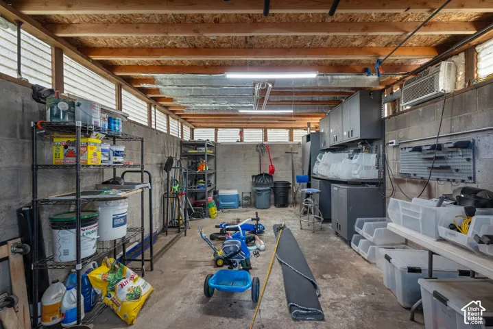 Concrete block garage featuring an exposed beam ceiling, built-in wall-mounted cabinetry, integrated wall-mounted storage panels, and high-intensity linear lighting