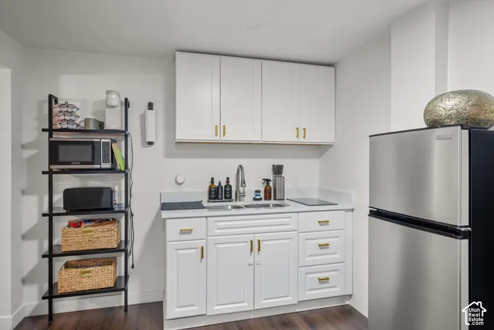 White cabinetry with gold-tone hardware, stainless steel refrigerator, stone-composite countertop, undermount sink with arched faucet, and wood-finish flooring