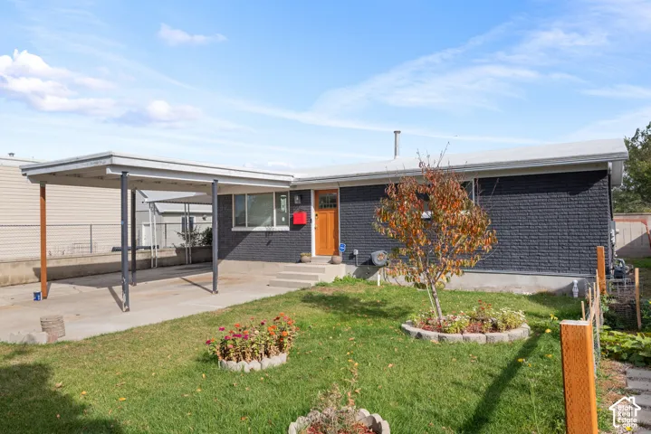 Painted brick exterior featuring a wood-panel front door, attached carport, concrete parking pad, and stone-bordered garden beds