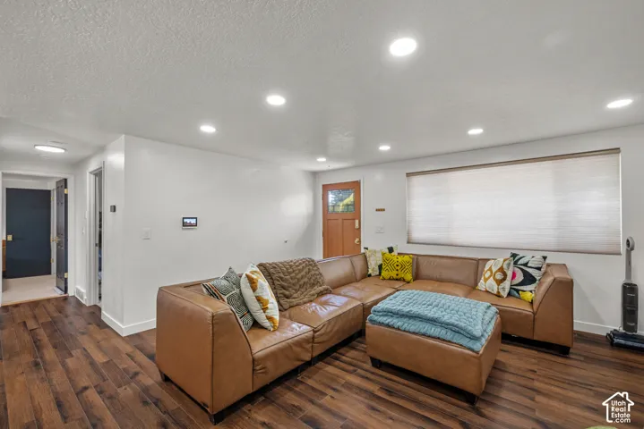 Living area featuring wood-finish flooring, recessed lighting, a multi-pane wood entry door, and a large picture window with integrated shade