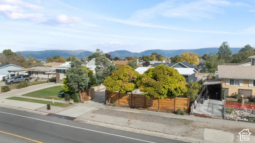 Aerial perspective featuring a wood-panel fence, mature trees, concrete driveway, and mountain backdrop