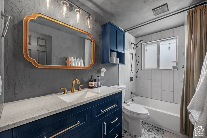 Bathroom featuring a navy blue vanity with gold-tone hardware, a solid-surface countertop with an integrated basin, a gold-framed decorative mirror, and patterned floor tile