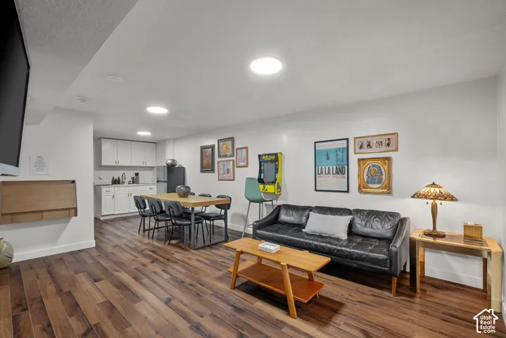 Open-concept space featuring wood-finish flooring, recessed lighting, and a kitchenette equipped with white cabinetry and a stainless steel sink