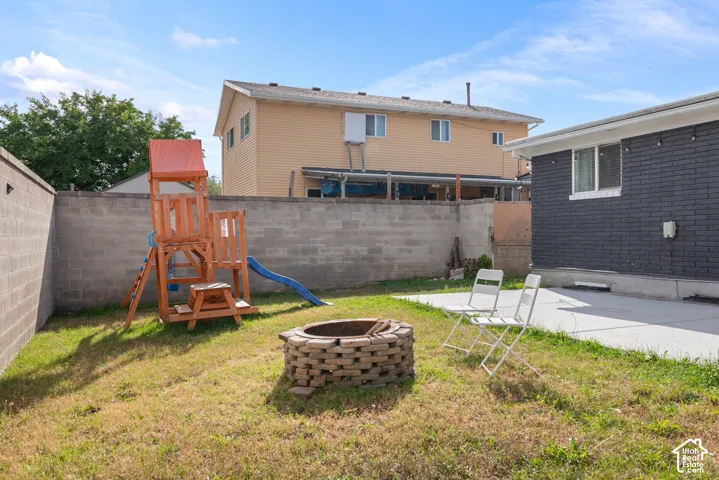 Backyard featuring a concrete patio, stone-surround fire pit, and perimeter masonry block wall