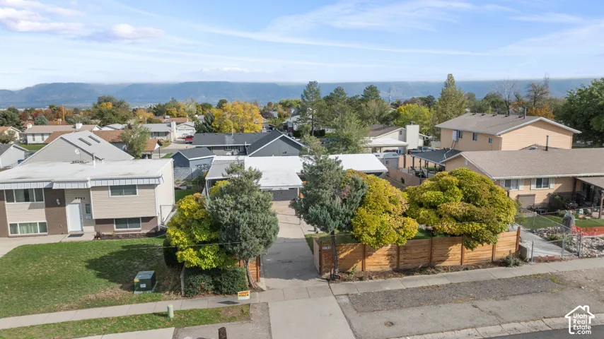 Aerial perspective of property featuring a concrete driveway, fenced perimeter, mature landscaping, and mountain backdrop