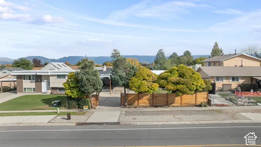 Exterior view featuring a horizontal wood-slat privacy fence, mature trees, concrete driveway, and mountain backdrop