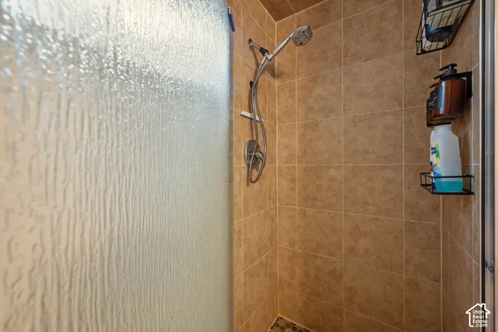 Shower enclosure featuring square-tiled wall surrounds, a hand-held shower head, a textured glass door, and a hexagonal-tiled shower floor