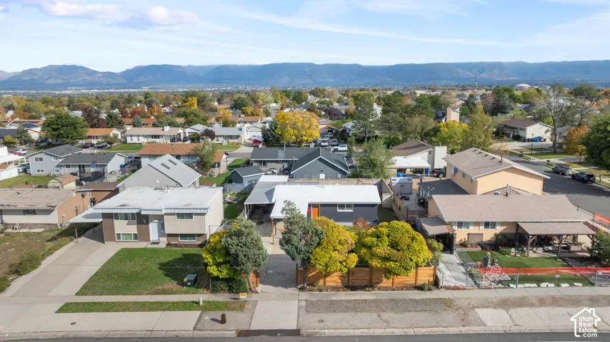 Aerial perspective featuring a low-profile residential structure with a covered front porch, horizontal wood-panel fencing, mature landscaping, and a prominent mountain range backdrop