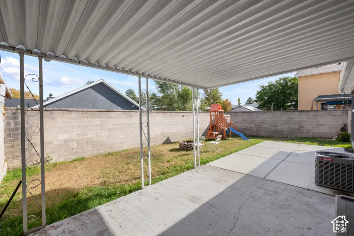 Covered concrete patio with decorative metal support posts, concrete block perimeter wall, and fenced backyard