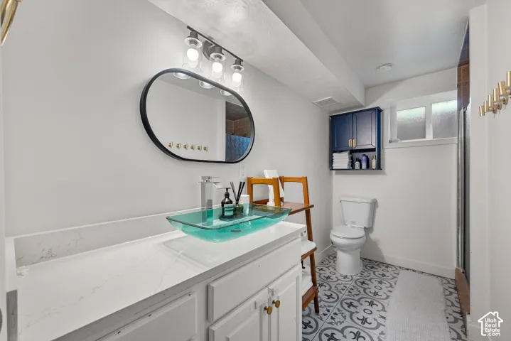 Bathroom featuring a vanity with a white composite countertop, a glass vessel sink, an oval-framed mirror, a mounted navy blue storage cabinet, and patterned tile flooring