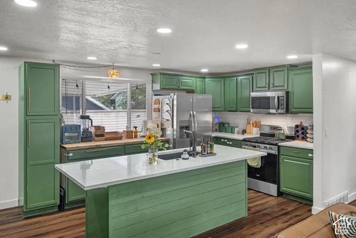Kitchen featuring custom green cabinetry, quartz countertops, a central island with a shiplap facade, wood-finish flooring, and stainless steel appliances
