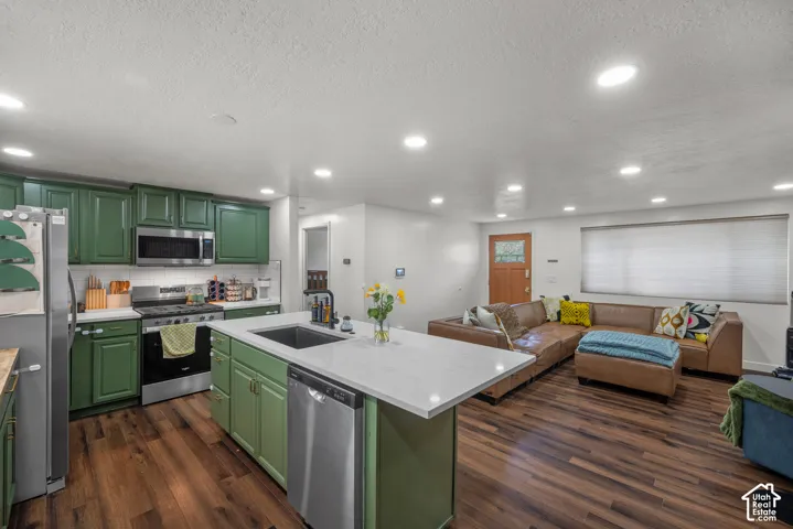 Kitchen featuring emerald-toned cabinetry, quartz countertops, a central island with an undermount sink, recessed lighting, and wood-finish flooring