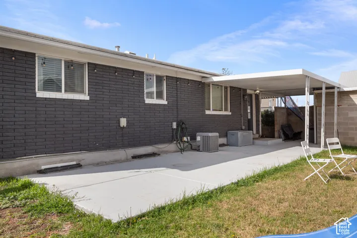 Dark-painted brick exterior featuring a concrete patio, covered carport, and multiple sliding windows