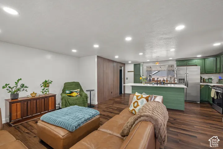 Open-concept kitchen and living area featuring wood-finish flooring, recessed lighting, a central island with a stone-finish countertop, and full-height wood paneling