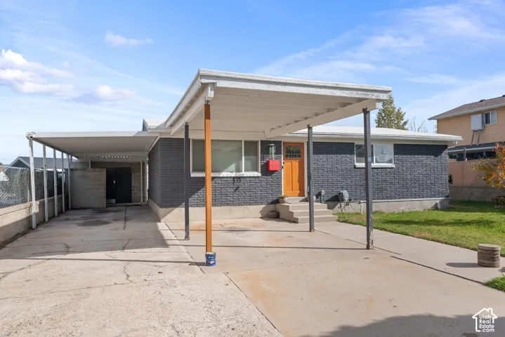 Exterior featuring a dark-painted masonry facade, an expansive covered carport, concrete driveway, and a solid wood front entry door with glass paneling