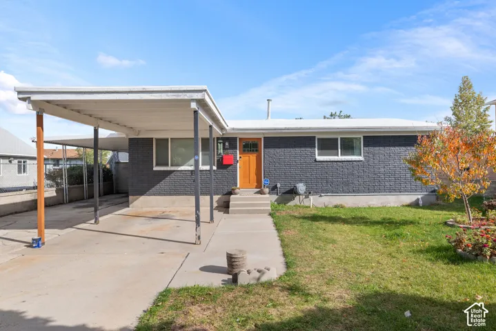 Single-story residence featuring a painted brick exterior, attached carport with support columns, concrete driveway, and an entryway with a glass-panel wood door