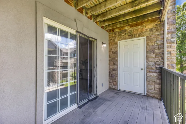 Private balcony featuring stone veneer siding, composite decking, six-panel exterior door, and sliding glass door with a mounted sconce